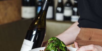 Serveuse tenant un plat et une bouteille de vin.