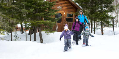 A family snowshoeing next to a cottage at Sommet Morin Heights.