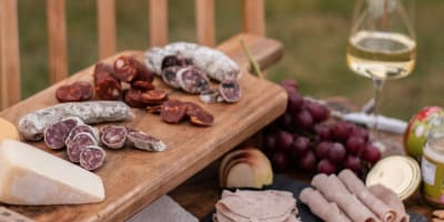 A platter of cold cuts and white wine on an outdoor table. 