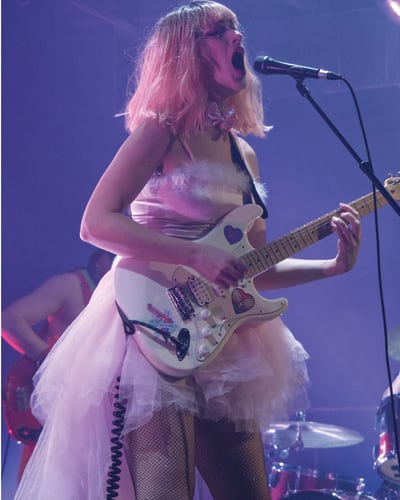 CEM - A woman in a pink dress is singing and playing electric guitar
