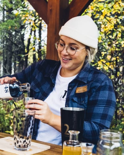 Distillerie du Fjord - Une femme prépare un breuvage alcoolisé, nature en arrière-plan.