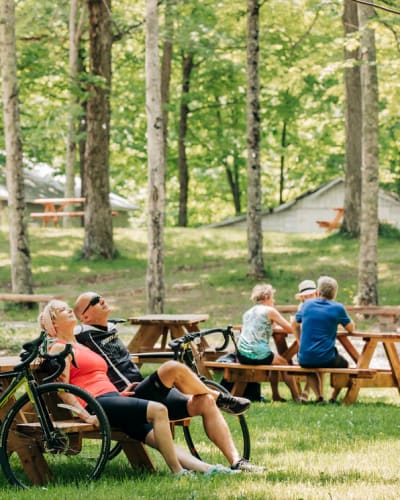 Érablière du Village - A man and a woman are seated at a picnic table, with their bikes leaning against it.