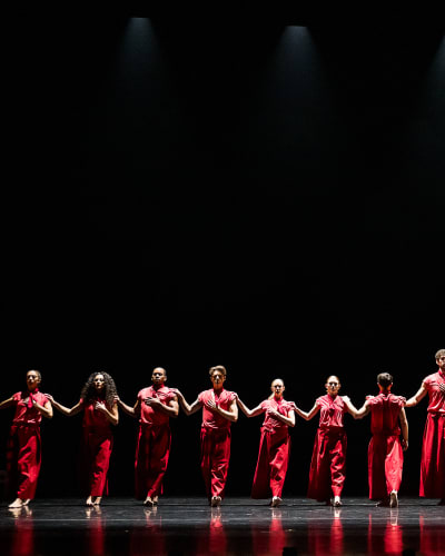 Festival des Arts de Saint-Sauveur - Des danseurs habillés en rouge sont disposés en ligne sur une scène noire