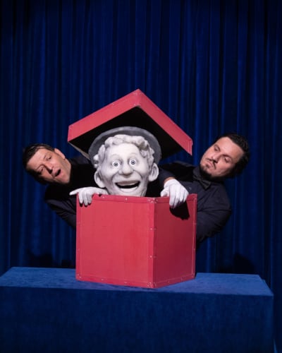 Festival international des arts de la marionnette - A puppet is in a red box. Two men stand next to it.