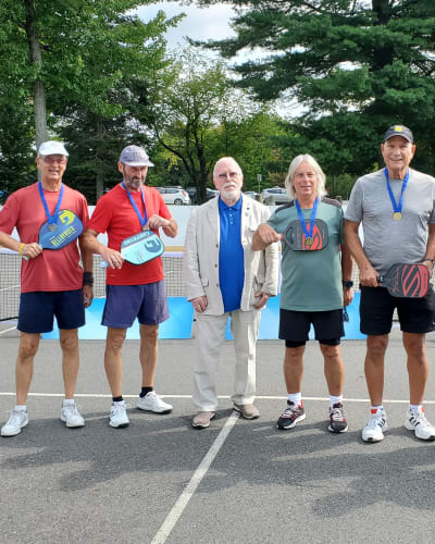 Jeux FADOQ provinciaux - On a pickleball court, there are six men wearing gold medals around their necks, and one man is dressed in a suit.