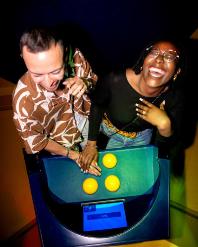 La Boîte à Questions – Quiz Room Montréal - Two people happily leaning over an interactive machine