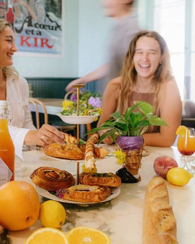La Midinette - Women sitting at a table filled with pastries and fruit