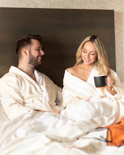 Couple relaxing in bed wearing bathrobes and enjoying a cup of coffee.