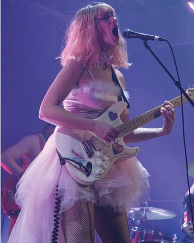 CEM - A woman in a pink dress is singing and playing electric guitar
