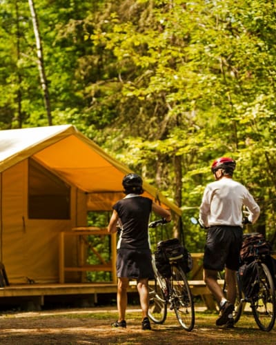 Un couple en vélo en direction d'un prêt-à-camper du Centre touristique du Lac-Kénogami.