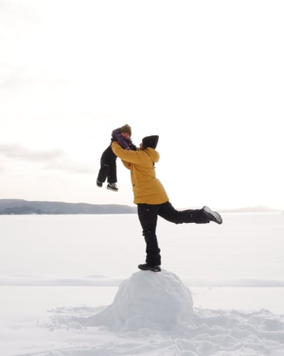 A parent holding their child in the air at the Centre touristique du Lac-Simon, in winter.