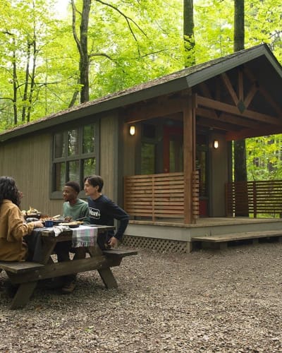 Des personnes assises à une table de pique-nique à côté d'un chalet au Parc national d'Oka.