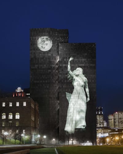 Cité Mémoire - Light projection of a woman and a moon on a large dark building, at night