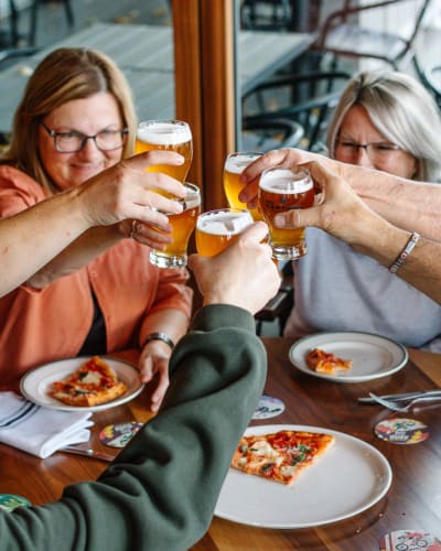 People around a table with pizza and beer from Des Cantons Microbrasserie.