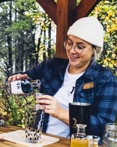 Distillerie du Fjord - A woman prepares an alcoholic beverage, nature in the background.