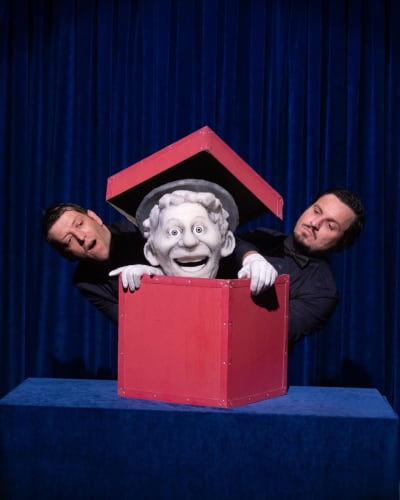 Festival international des arts de la marionnette - Une marionnette est dans une boîte rouge. Deux hommes sont à côté.