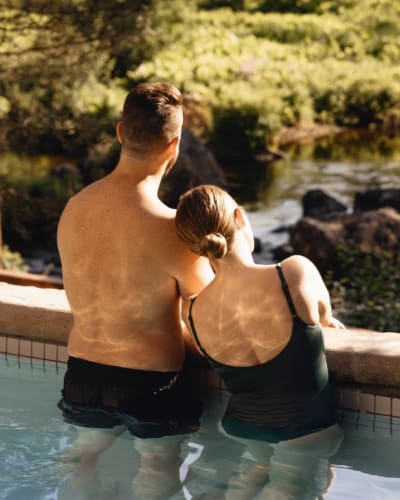 A couple relaxing in an outdoor pool surrounded by nature.