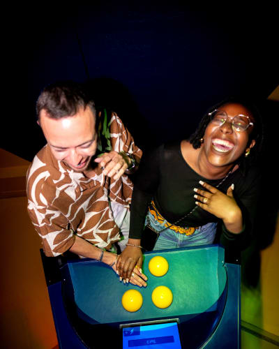 La Boîte à Questions – Quiz Room Montréal - Two people happily leaning over an interactive machine
