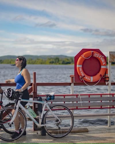 A man and a woman are standing beside the water, with their bicycles at their sides.