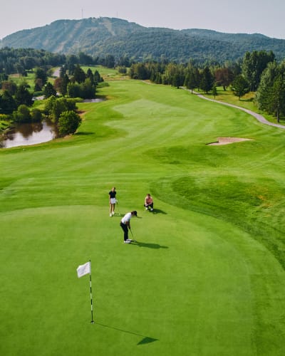 Three people on the green at Golf Château-Bromont, with the mountain in the background.