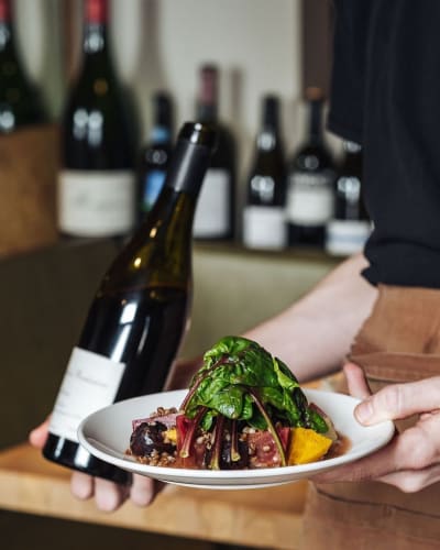 Serveuse tenant un plat et une bouteille de vin.