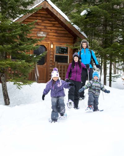 A family snowshoeing next to a cottage at Sommet Morin Heights.