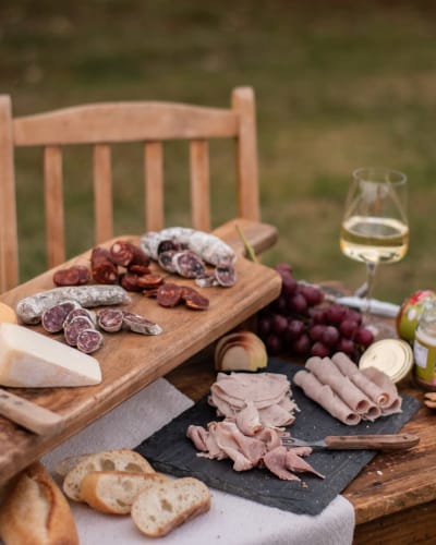 A platter of cold cuts and white wine on an outdoor table. 