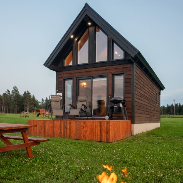 Grand chalet vitré avec feu de camp et table à picnic sur le terrain.