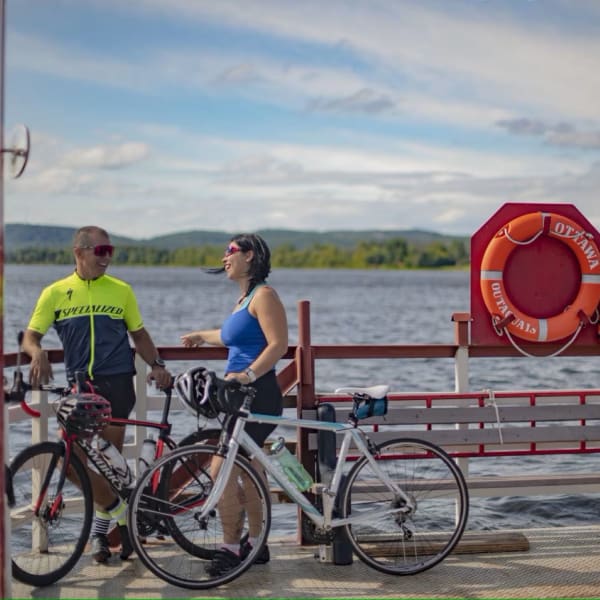 A man and a woman are standing beside the water, with their bicycles at their sides.