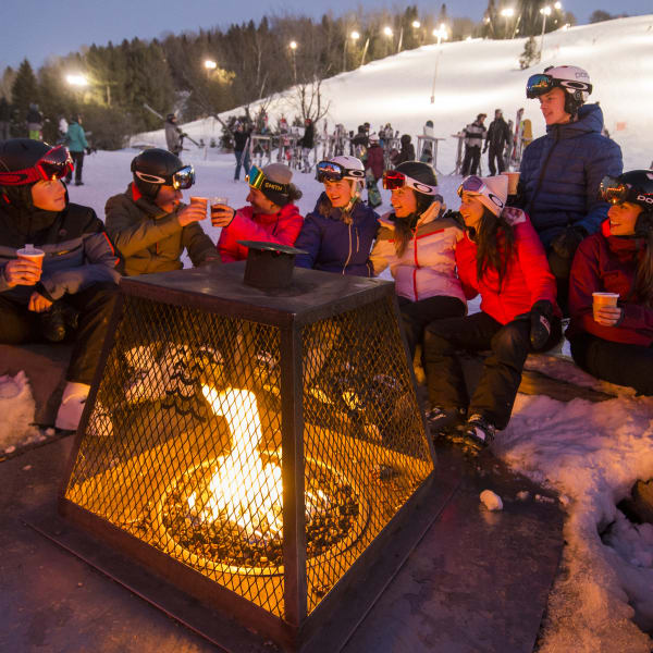 Groupe d'ami·es autour d'un feu extérieur au pied des pentes de ski.