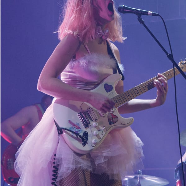 CEM - A woman in a pink dress is singing and playing electric guitar