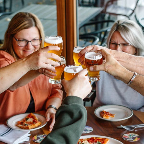 People around a table with pizza and beer from Des Cantons Microbrasserie.