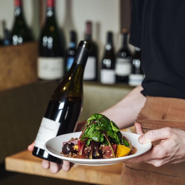 Waitress holding a plate and a bottle of wine.