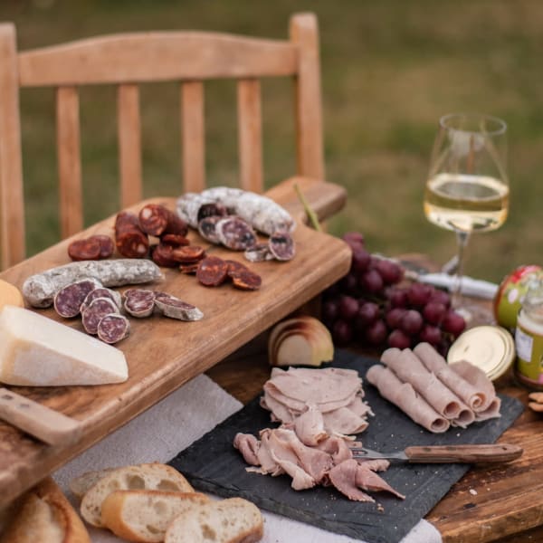 A platter of cold cuts and white wine on an outdoor table. 