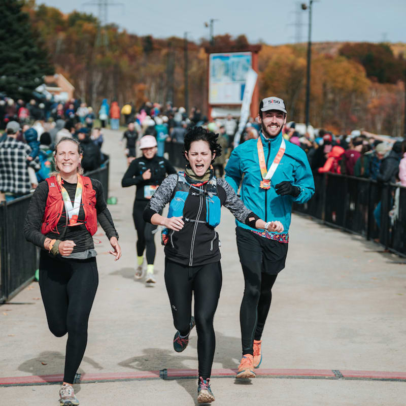 Défi des Couleurs Simard - Trois personnes franchissent la ligne d'arrivée d'une course, avec une foule en arrière-plan.