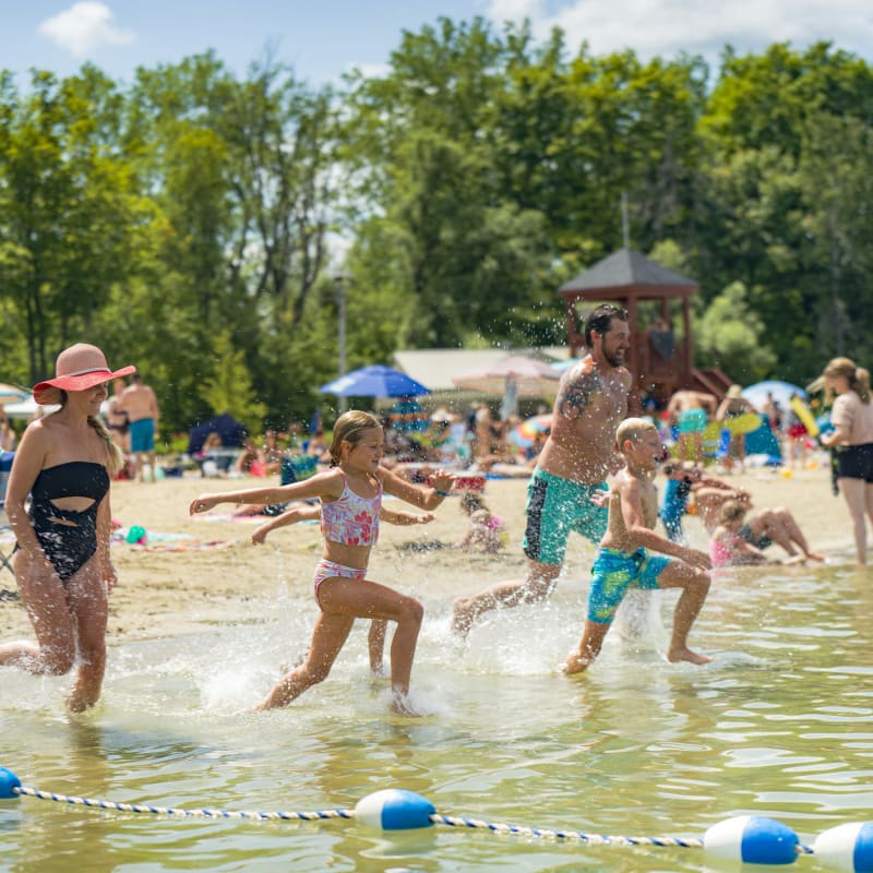 Family running toward the water at the beach in Îles-de-Saint-Timothée Regional Park