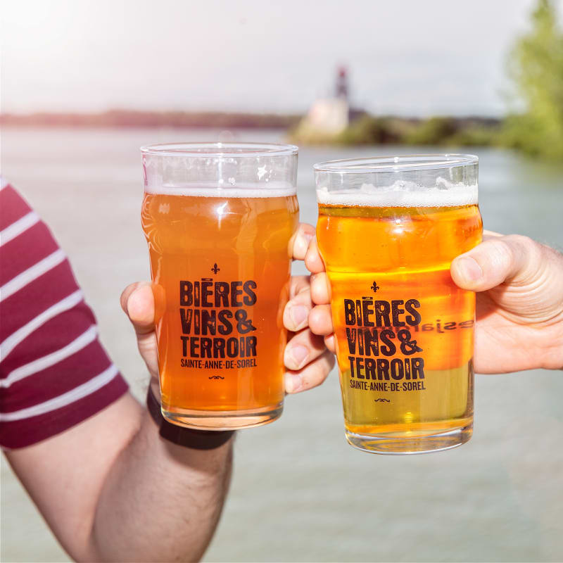 Deux mains qui trinquent avec des bières au bord de l'eau.
