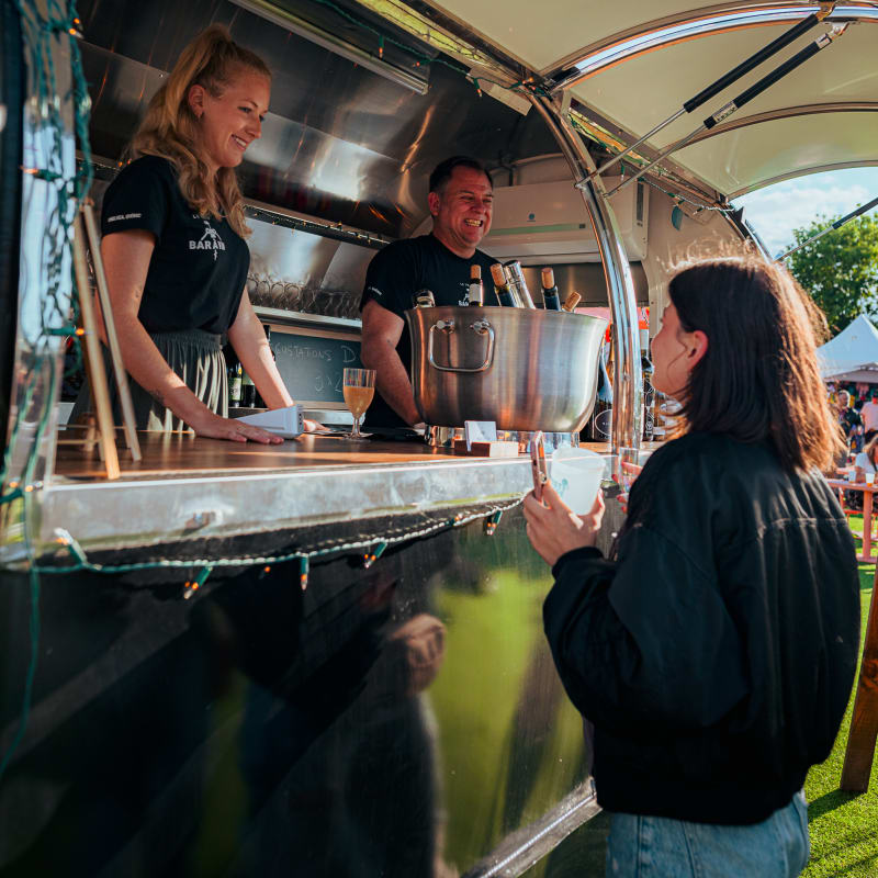 Festival Parasol - A woman chats with two smiling vendors in a mobile bar.