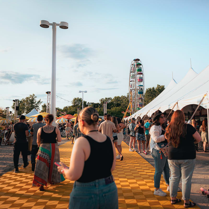 Festival Parasol - People are scattered around the site. A large white tent is on the right, with a Ferris wheel in the background.