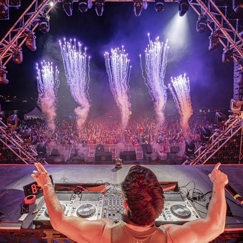 Riverside Festival - DJ on stage in front of a festive crowd, with pyrotechnics.