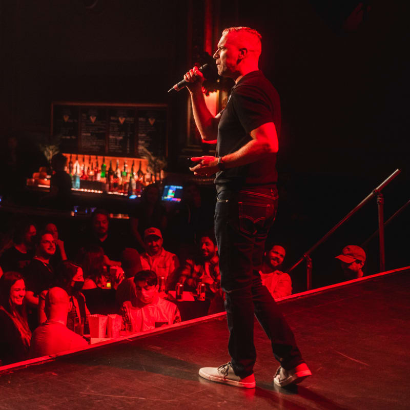 Festival SPASM - Sur une scène, un homme est en train d'utiliser un microphone, les spectateurs se trouvent en arrière-plan.