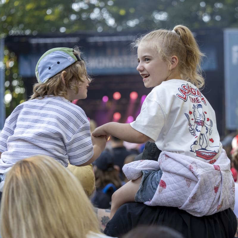 Two young people on the shoulders of others in the festival crowd.