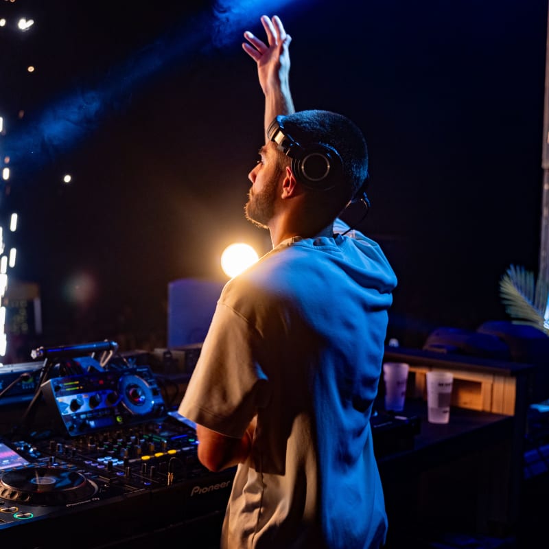 M DGTL - Un DJ se tient devant son équipement, la main vers le ciel.
