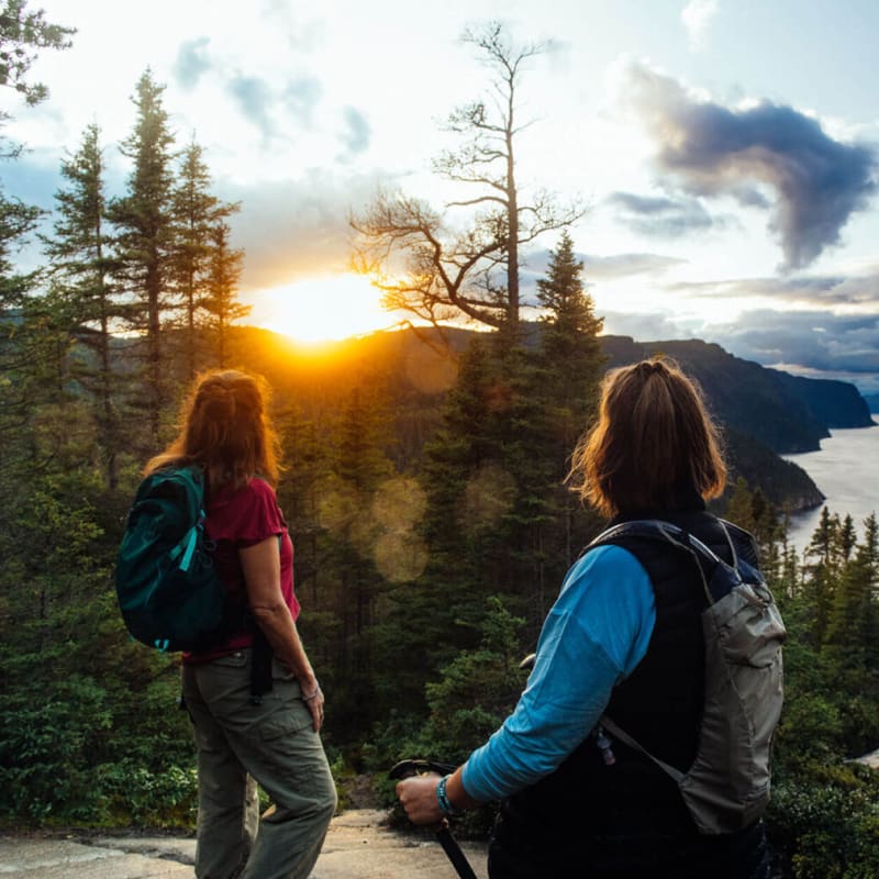 Parc national du Fjord-du-Saguenay - Two women on top of a mountain, forest and sunset in the background.