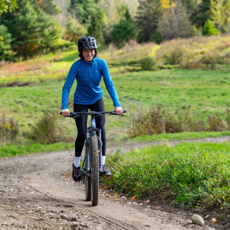 A woman on a bicycle on a dirt path in an early autumn setting.