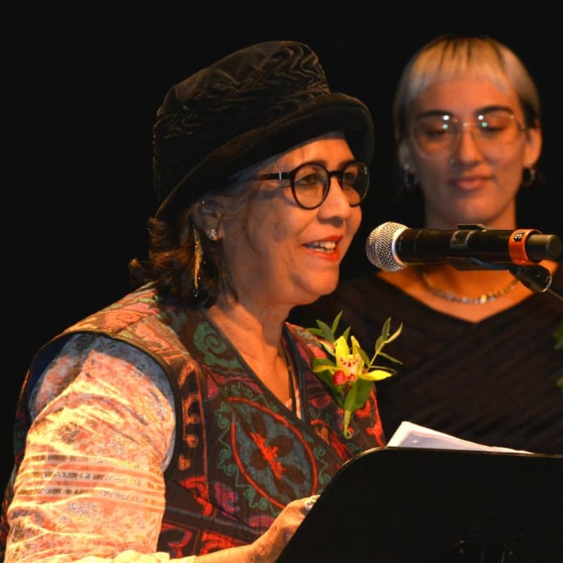 Une femme qui devant un micro et un podium récite un poem et une jeune femme se tient à côté d'elle.