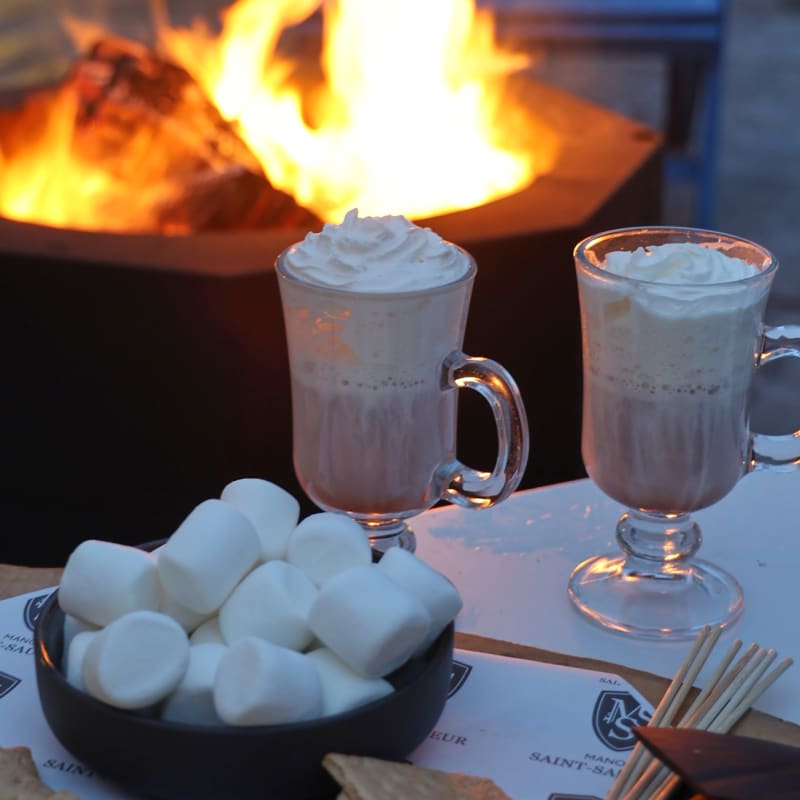 Outdoor firepit with two mugs of hot cocoa and ingredients to make s'mores.