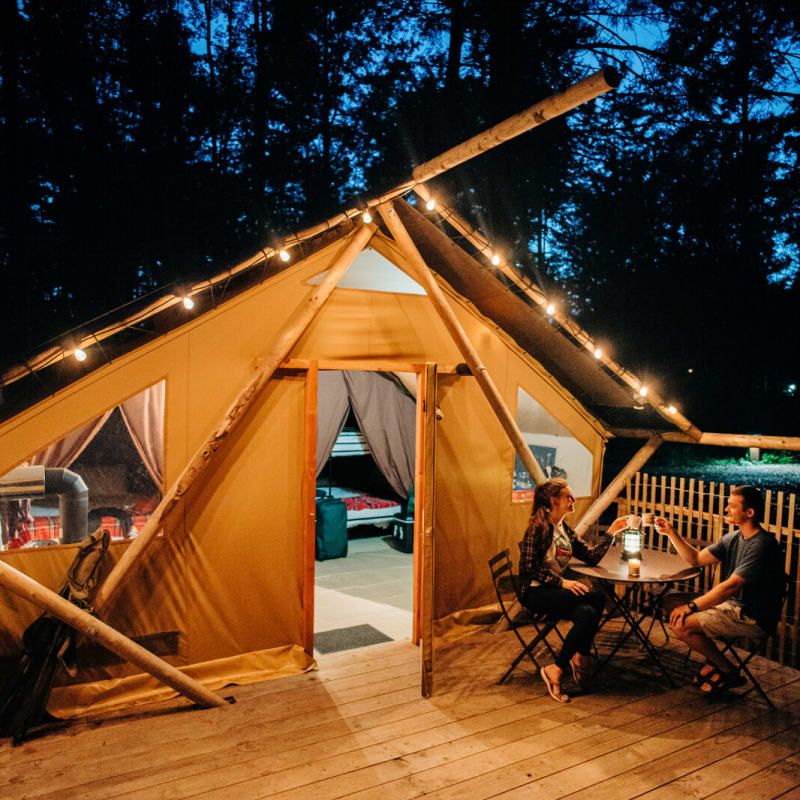 Two people are sitting on the terrace of a ready-to-camp tent at dusk.