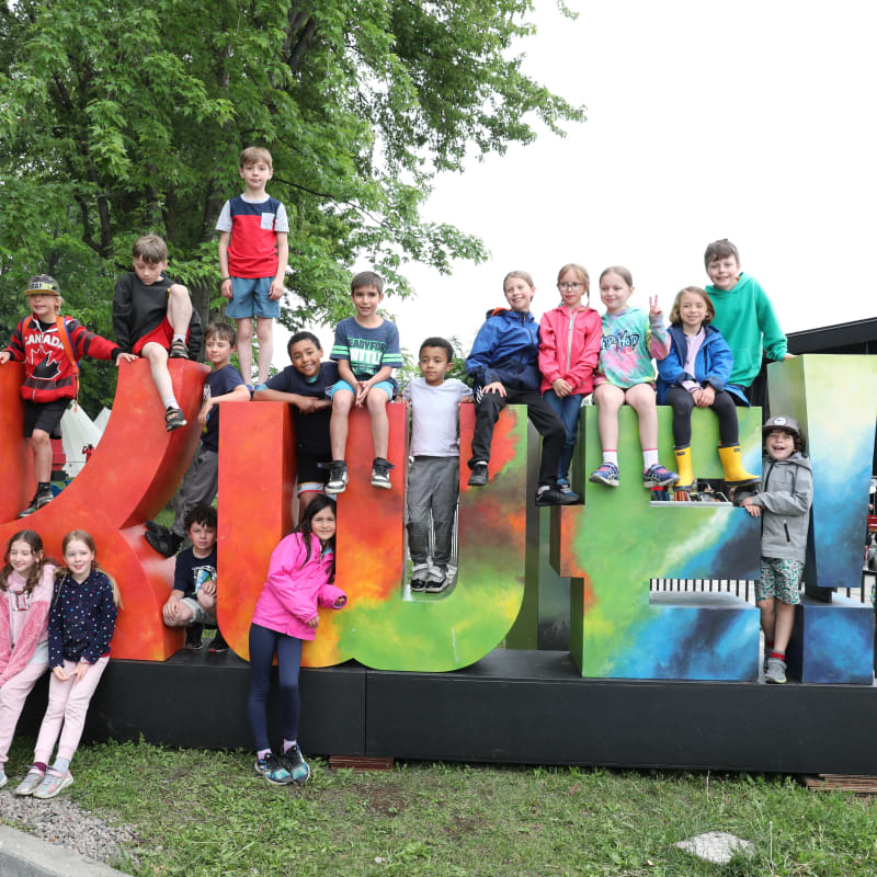 Children around the giant logo of the Kwe Festival.