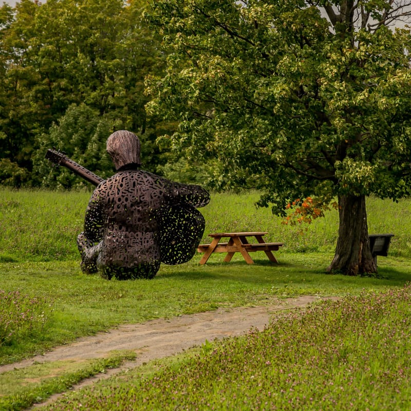 Sculpture représentant Félix Leclerc et paysage côtier de l'ile d'orléans.